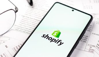 Shopify logo on phone against backdrop of bills