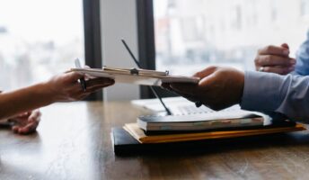 A recruiter hands a clipboard to a worker